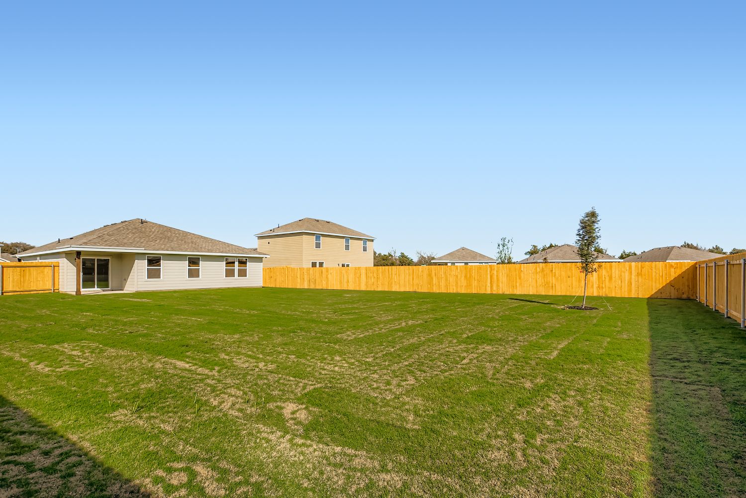 A large green field with a fence and a house in the background.